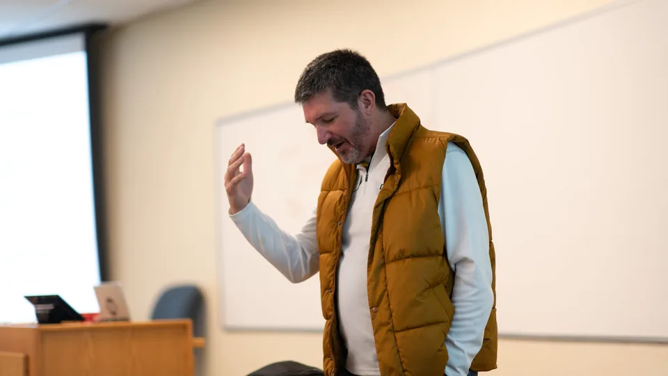 Matthew Beimers with a hand raised, making a point in class
